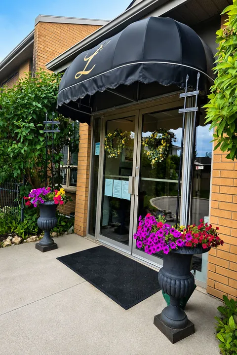 Entrance door beneath a dark awning, beside flower planters.