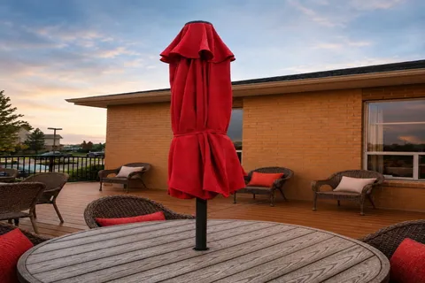 Patio with wicker chairs, a table and a closed red umbrella.