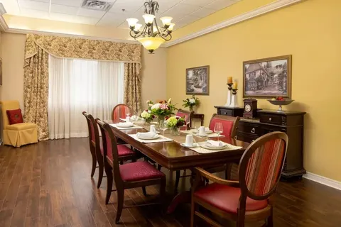 Long dining table with red chairs and framed cottage paintings