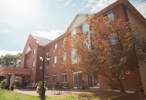 Red brick building with a covered entrance, patio chairs, trees and lawn