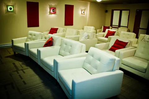 TV room with rows of white armchairs and red cushions.