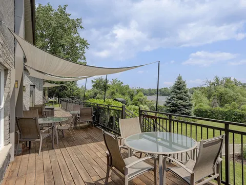 Wooden terrace with tables, chairs and a shade sail beside the building