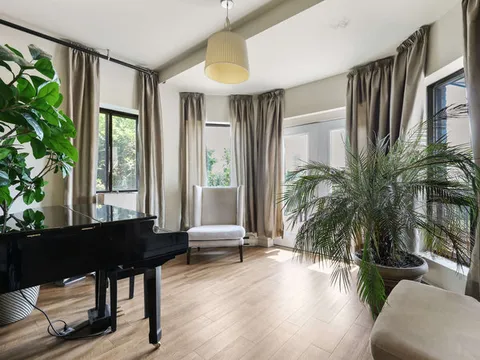 Windowed room with a grand piano, armchairs and potted plants