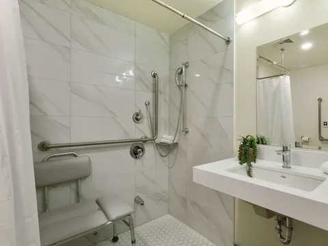 Bathroom with a shower seat, grab bars, sink and wall mirror