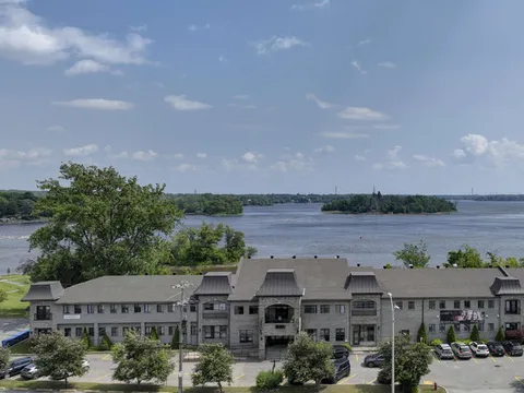 Residence beside a river with trees, a driveway and parked cars