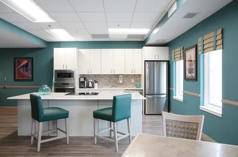 Room with dining tables, a white kitchen island and teal stools
