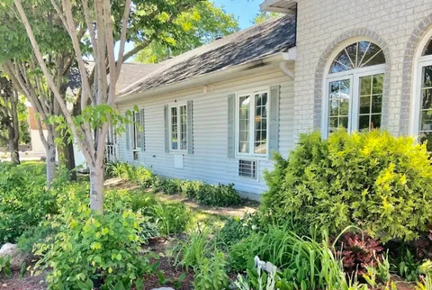 Low building with white siding, arched windows, trees and garden plants