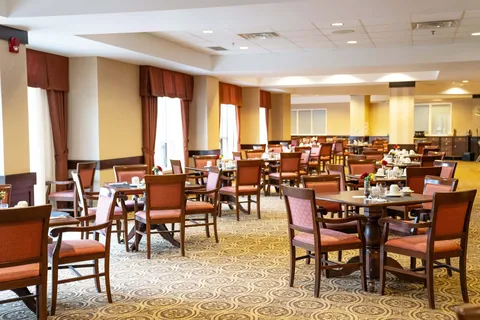 Dining room with rows of tables and upholstered chairs beside tall windows