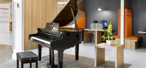 Black grand piano beside orange booth seating and a computer desk