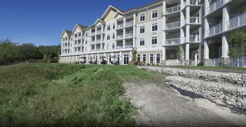 Multi-storey building with balconies above a grassy riverbank and patio