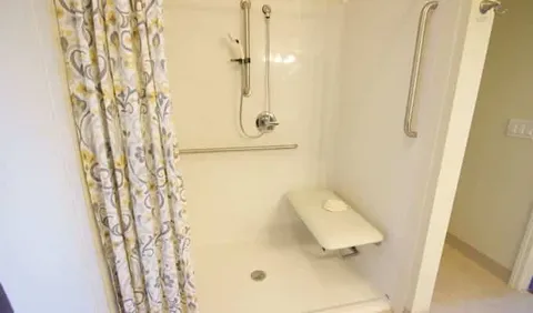 Bathroom with a shower seat, grab bar and patterned shower curtain