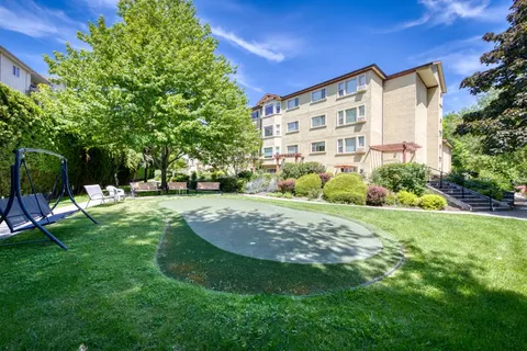 Residence building overlooking a lawn, trees and an outdoor games court.