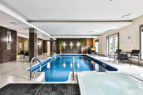 Indoor swimming pool and hot tub with tiled surrounds, metal handrails and chairs