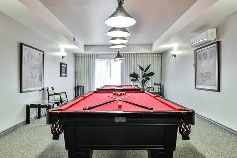 Billiards room with two red pool tables, pendant lights and framed wall art