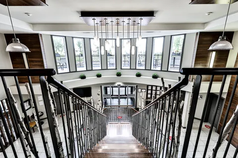 View down a wooden staircase into a tall lobby with large windows and glass entrance doors
