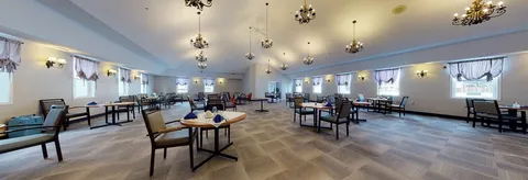 Dining room with spaced tables, chairs, chandeliers and large windows.