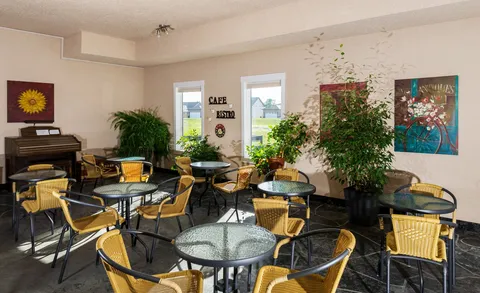 Bistro seating with glass tables, wicker chairs, plants and a piano.