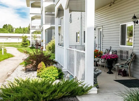 Covered porch with outdoor chairs, flowerpots and garden beds.