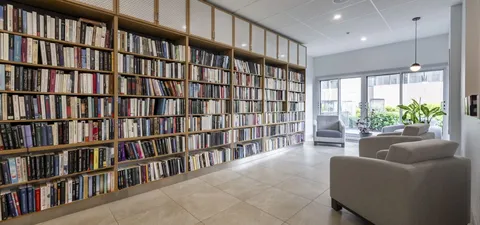 Library with tall wooden bookcases and grey armchairs beside windows
