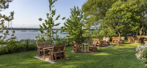 Wooden garden seating beside trees and a railing overlooking a river
