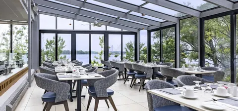 Dining room with set tables and dark chairs beside broad windows