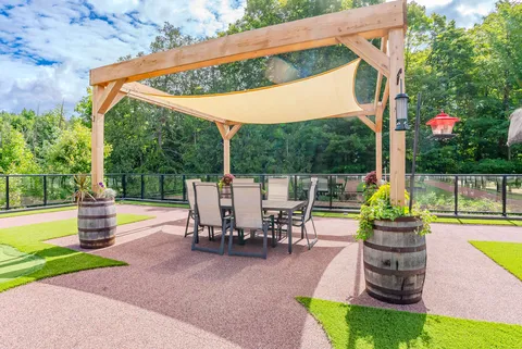 Patio table and chairs beneath a fabric shade supported by wooden posts