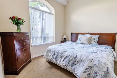 Bedroom with patterned bedding, wooden drawers and an arched window