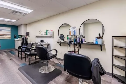 Salon chairs beneath round mirrors beside hair dryers and counters