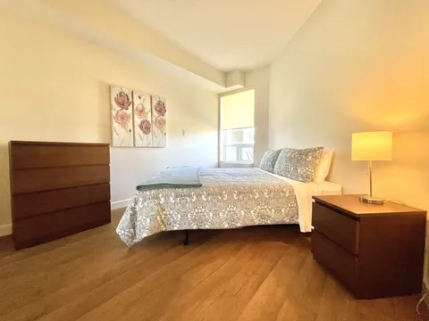 Bedroom with a bed and wooden dressers beside a window.