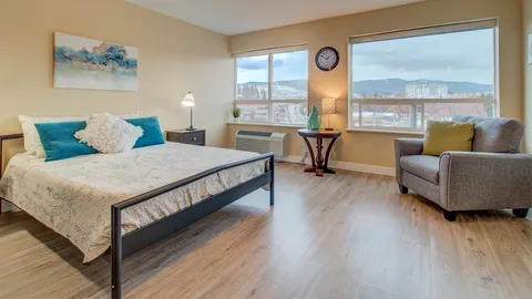 Studio suite with a bed, kitchenette and sitting area beside a window.
