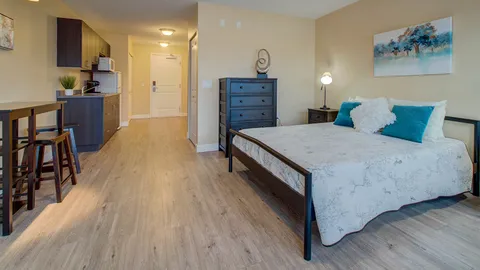Suite with a bed, dresser and kitchenette along the entry corridor.