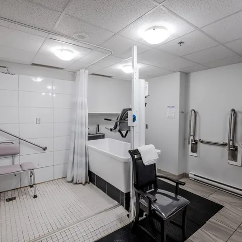 Tiled bathing room with a bathtub, lift, shower chair and wall grab bars