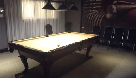 Billiards room with a pool table, overhead lamps and chairs along the wall