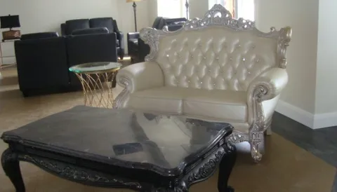Sitting room with a cream tufted sofa, dark armchairs and glass coffee tables