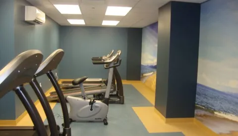 Fitness room with exercise bicycles and treadmills beside beach murals