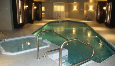 Indoor pool with steel handrails, a small spa pool and wall lights