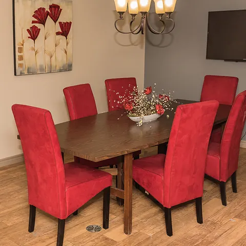 Room with a wooden dining table, red chairs, a floral painting and television