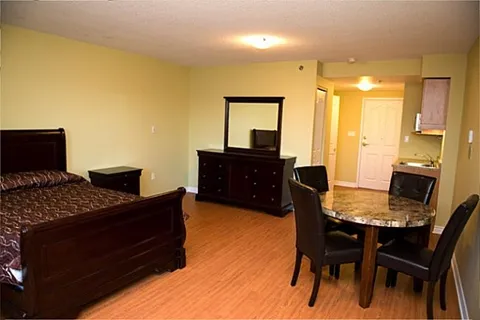 Bedroom with a wooden bed, dresser, mirror and a kitchen area