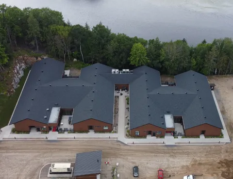 Aerial view of a low brick residence beside a lake and trees