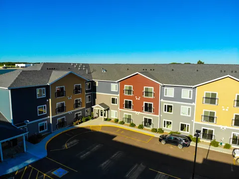 Residence facade with colourful siding, windows, an entrance and a parking area.