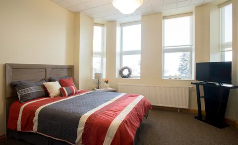 Bedroom with a double bed, large windows and a television.
