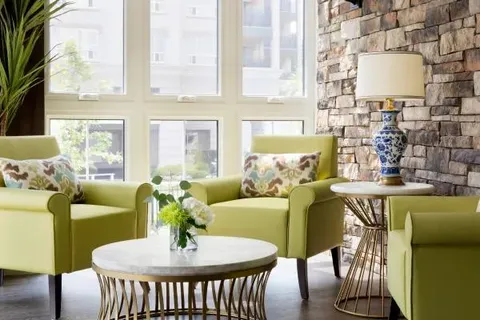 Lounge chairs beside tall windows and a stone wall.
