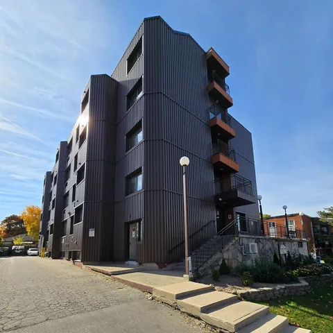 Multi-storey building with grey siding, balconies, outdoor steps and planted flower beds