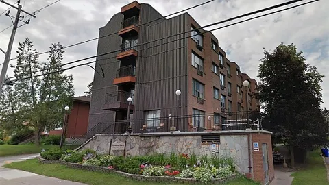 Brick and grey-sided building with balconies, a raised terrace and flower beds beside the sidewalk