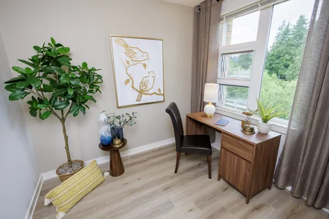 Desk and chair beside a window, potted plant and bird artwork