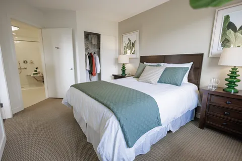 Bedroom with a bed, bedside lamps and open closet and bathroom doorways
