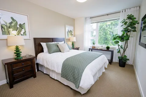 Bedroom with a bed, pale green quilt, bedside cabinets and large windows