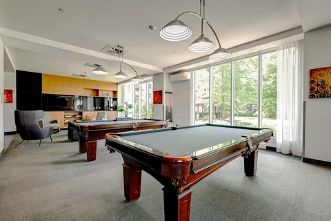 Two billiards tables beneath pendant lights beside large windows