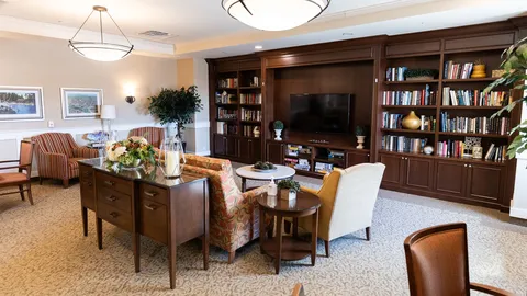 Armchairs beside wooden bookshelves, a television and round tables