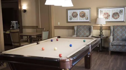 Pool table beside patterned armchairs and framed floral prints
